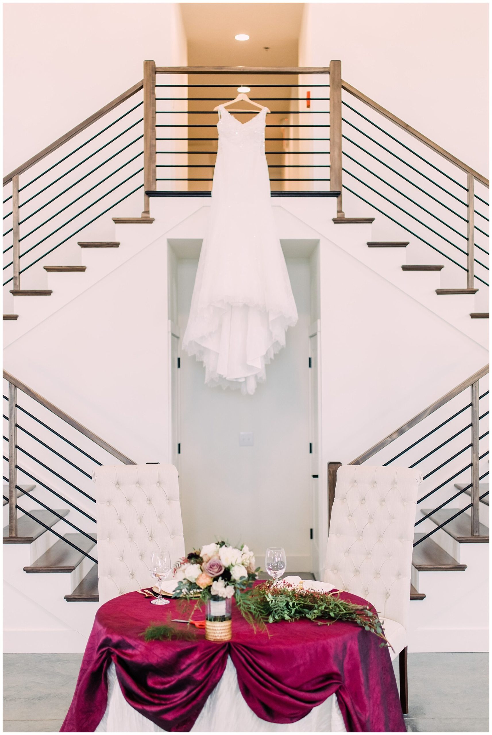 wedding sweetheart table with wedding gown behind it hanging on stairs