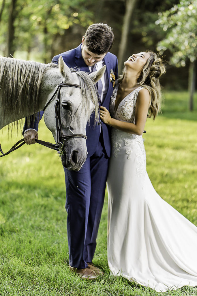 bride and groom standing with a horse laughing in the sunset
