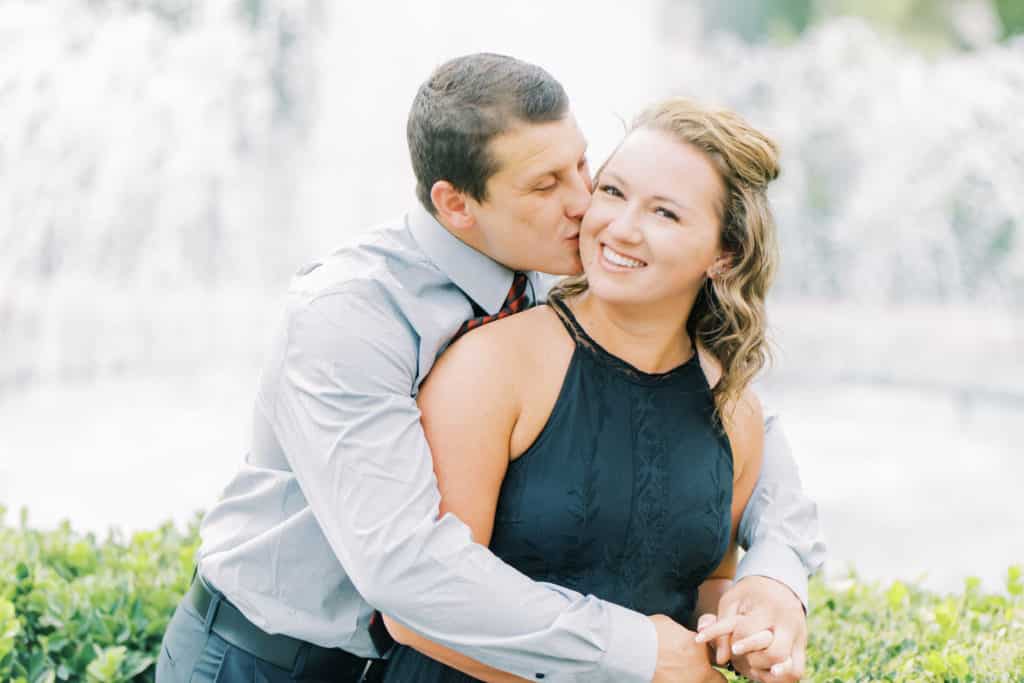 woman being kissed by man on cheek in front of fountain